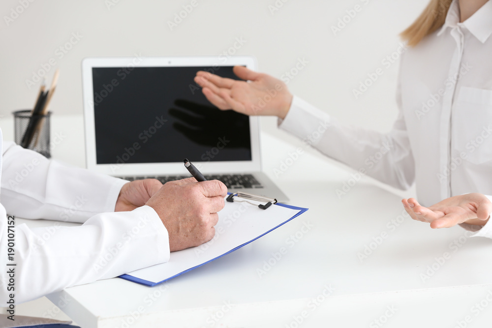 Male doctor filling up application form while consulting patient in clinic, closeup Male doctor filling up application form while consulting patient in clinic, closeup