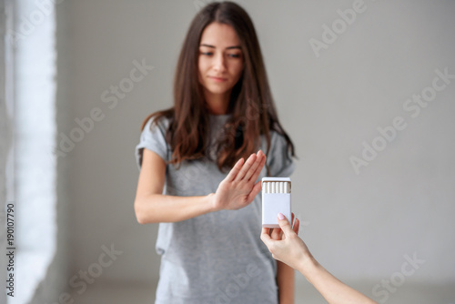 Fototapeta Naklejka Na Ścianę i Meble -  No smoking. Healthy young beautiful girl refusing to take cigarette from package. Portrait of female showing stop sign with hand to cigarettes. Quit smoking, health care concept.