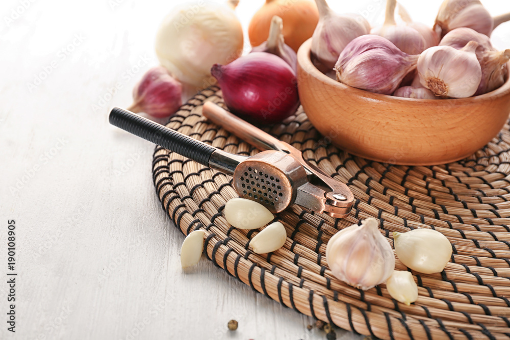 Garlic crusher and cloves on wicker mat, closeup Garlic crusher and cloves on wicker mat, closeup