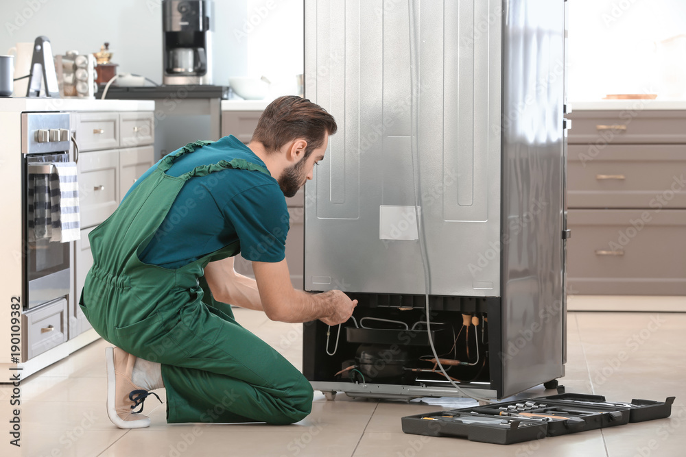 Male technician repairing refrigerator indoors Male technician repairing refrigerator indoors
