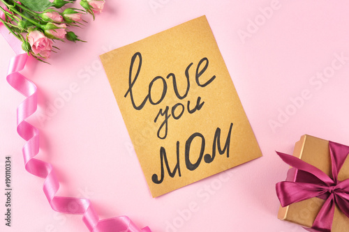 Card with text "LOVE YOU MOM", flowers and gift box on color background. Greetings for Mother's day