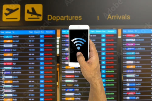 Hand holding a phone with wifi logo on timetable flight board in background