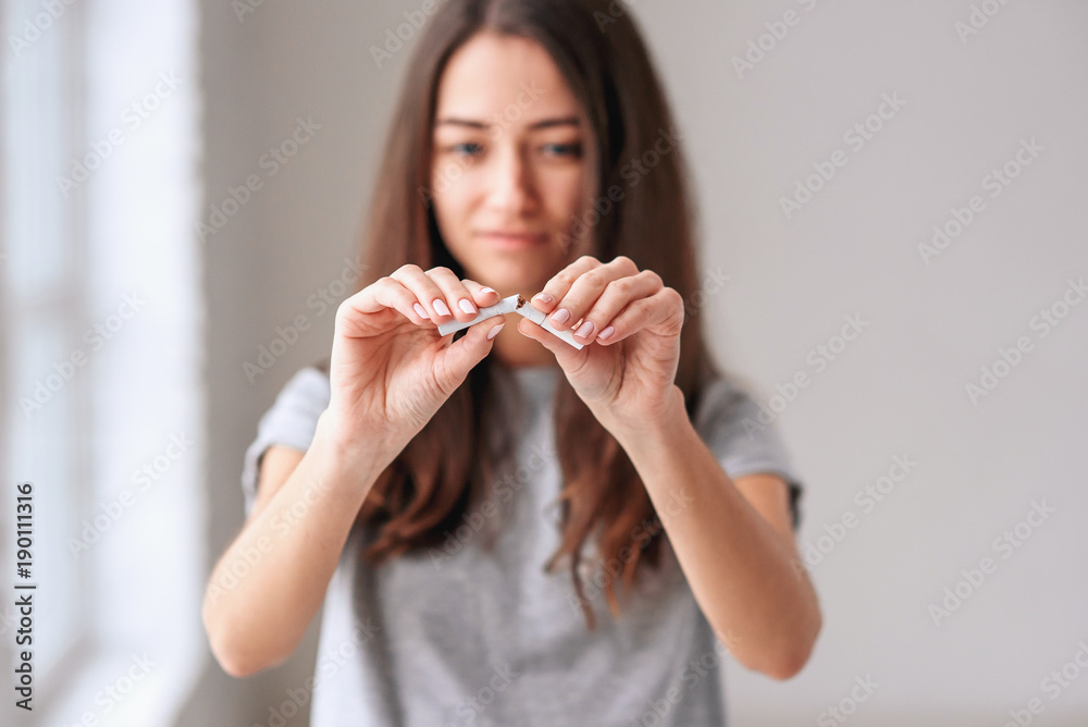 Stop smoking cigarettes concept. Portrait of beautiful smiling girl holding broken cigarette in hands. Happy female quitting smoking cigarettes. Quit bad habit, health care concept. No smoking. Stop smoking cigarettes concept. Portrait of beautiful smiling girl holding broken cigarette in hands. Happy female quitting smoking cigarettes. Quit bad habit, health care concept. No smoking.