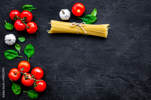 Cook spaghetti with tomatoes, garlic, basil. Italian recipe. Black wooden background top view copy space