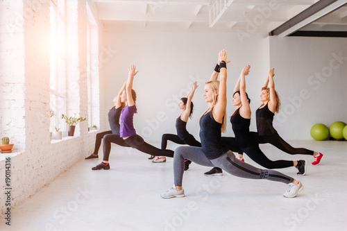 Group of women doing yoga, pilates and fitness and exercise indoors in white loft interior studio.