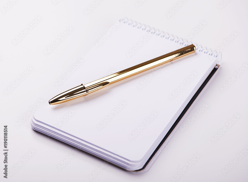 Notepad with blank paper next to golden ball pen on white background. Isolated. Mockup. Notepad with blank paper next to golden ball pen on white background. Isolated. Mockup.