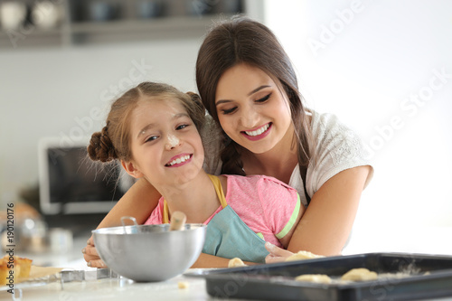 Mother and daughter with cookie dough at table indoors
