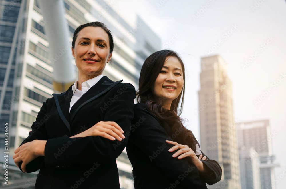 two smiling business asian and caucasian woman in formally dressed looking into camera with her arms crossed standing in modern city, confident, team leader, successful and entrepreneurship concept two smiling business asian and caucasian woman in formally dressed looking into camera with her arms crossed standing in modern city, confident, team leader, successful and entrepreneurship concept