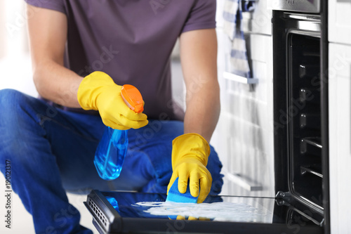 Man cleaning oven in kitche...