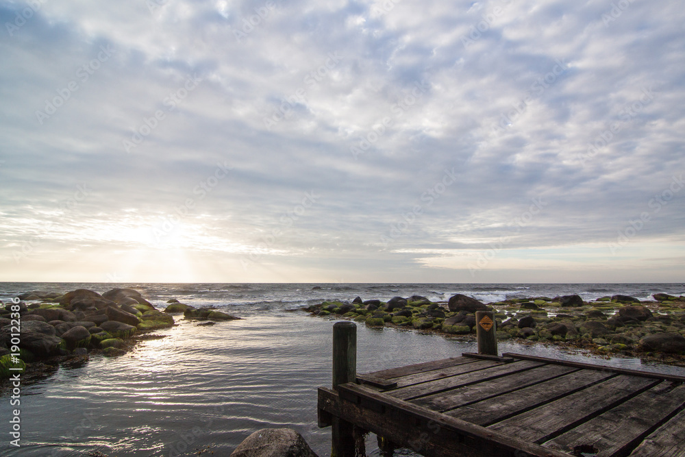 Idyllischer Sonnenuntergang mit Sonnenstrahlen an kaputtem Steg am Meer