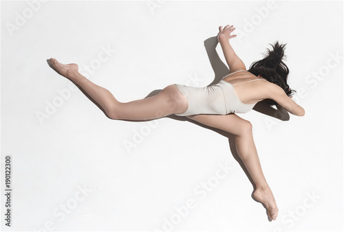 Young beautiful dancer in beige dress dancing on gray background