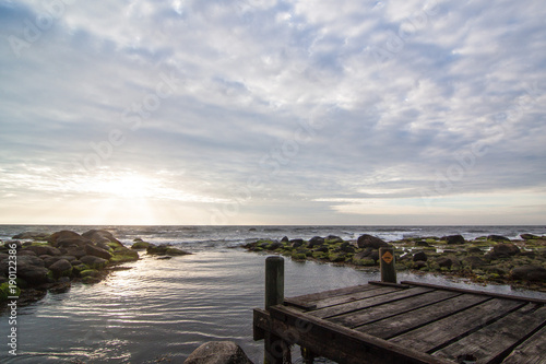 Idyllischer Sonnenuntergang mit Sonnenstrahlen an kaputtem Steg am Meer