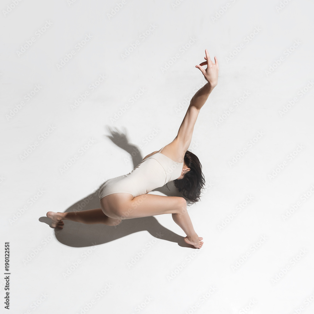 Obraz premium Young beautiful dancer in beige dress dancing on gray background