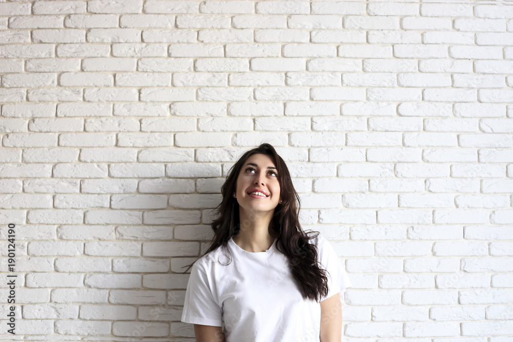 Happy millennial girl having fun indoors. Portrait of young woman with diastema gap between teeth. Beautiful smile. Minimalistic interior, white brick textured wall background, loft style. Copy space.