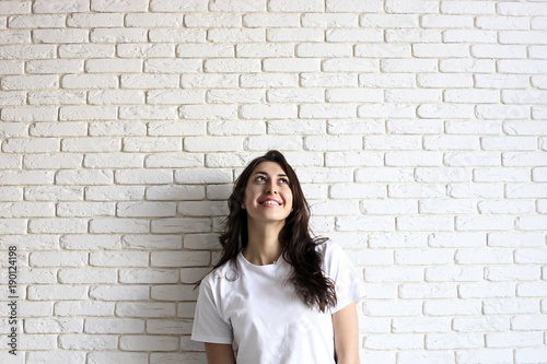 Happy millennial girl having fun indoors. Portrait of young woman with diastema gap between teeth. Beautiful smile. Minimalistic interior, white brick textured wall background, loft style. Copy space.