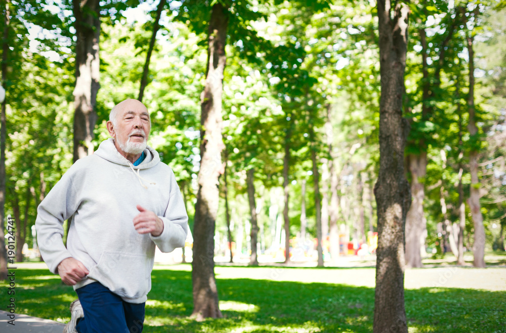 Fototapeta premium Elderly man running in green park, copy space