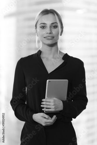Beautiful business woman with tablet in hands stands near window in office. photo