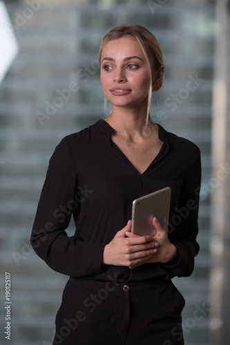 Beautiful business woman with tablet in hands stands near window in office. photo