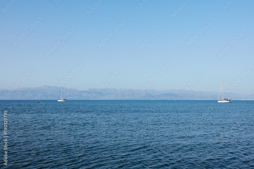 Fantastic seaside view at the sea with the two yachts on the horizon, Corfu island, Greece. Sunny day, minimalism, calm and silence.