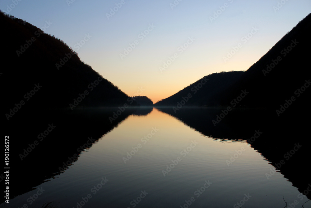 Perfect symmetrical reflection of mountain silhouette on a flat lake surface at dusk