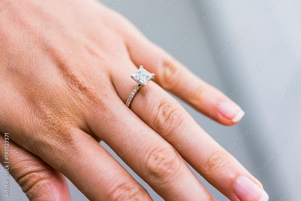 Macro closeup of princess cut diamond engagement ring on woman's female hand showing detail and texture Macro closeup of princess cut diamond engagement ring on woman's female hand showing detail and texture