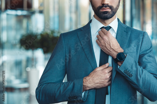 Businessman in a fromal suit in a business center tighten a tie close-up