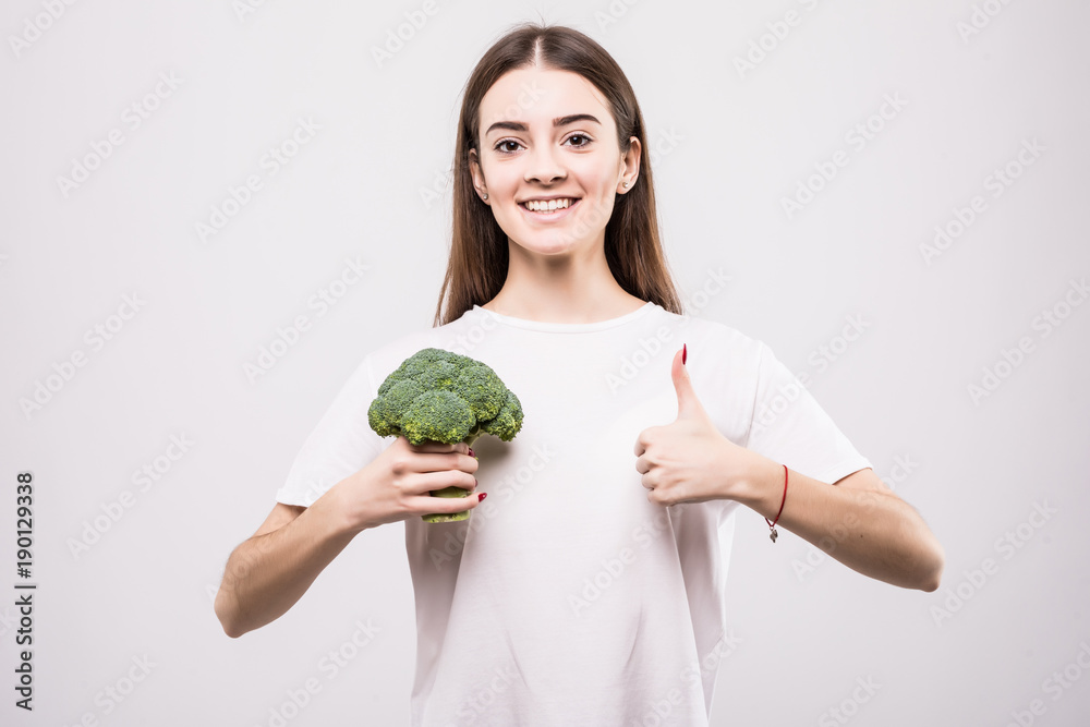 Portrait of a cheerful pretty girl holding broccoli and showing thumbs up gesture isolated over white background. Health concept. Portrait of a cheerful pretty girl holding broccoli and showing thumbs up gesture isolated over white background. Health concept.