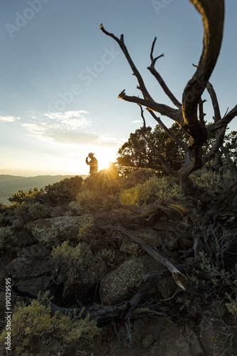 A cowboy tips his hat on top of a mountain as golden rays from the sun shine behind him.