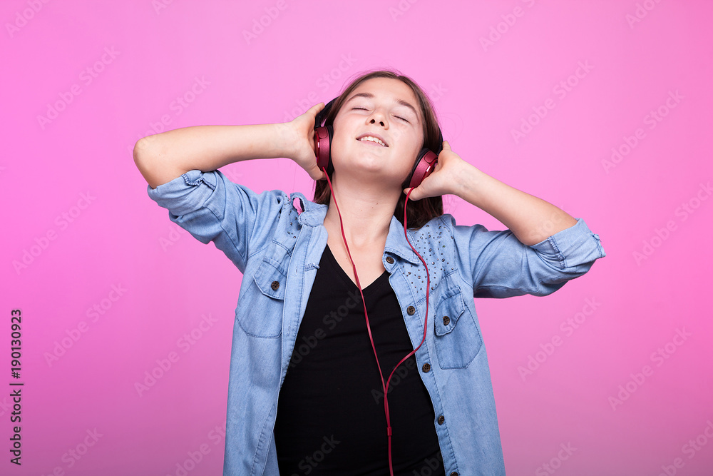 Young teenager girl enjoying music with headphones on head on pink background in studio photo Young teenager girl enjoying music with headphones on head on pink background in studio photo