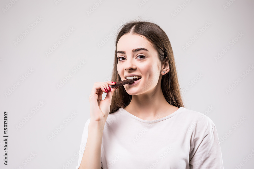 health, people, food and beauty concept - Lovely smiling teenage girl eating chocolate isolated on gray background health, people, food and beauty concept - Lovely smiling teenage girl eating chocolate isolated on gray background