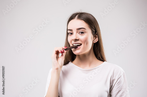 health  people  food and beauty concept - Lovely smiling teenage girl eating chocolate isolated on gray background