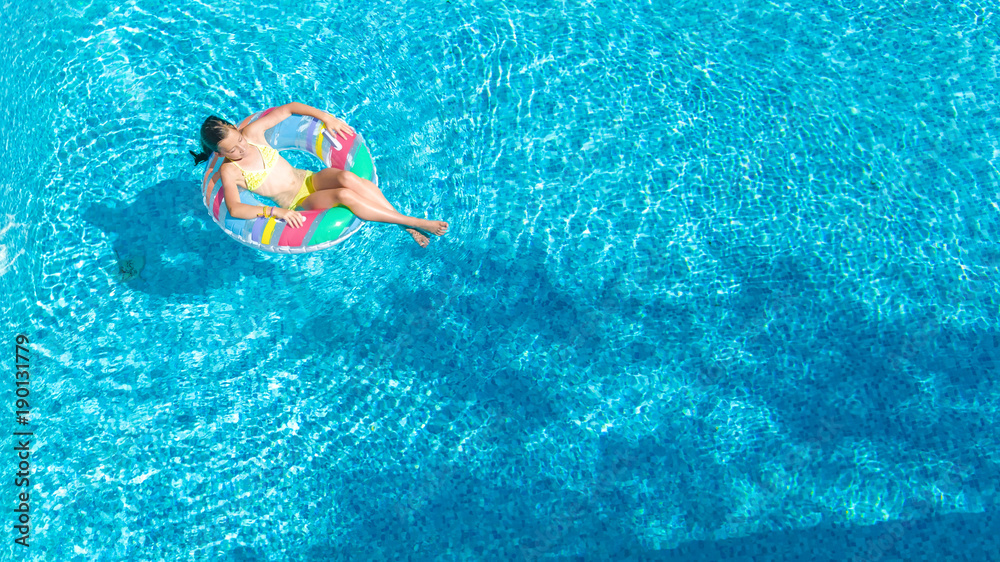 Aerial top view of little girl in swimming pool from above, kid swims on inflatable ring donut , child has fun in water on family vacation resort
