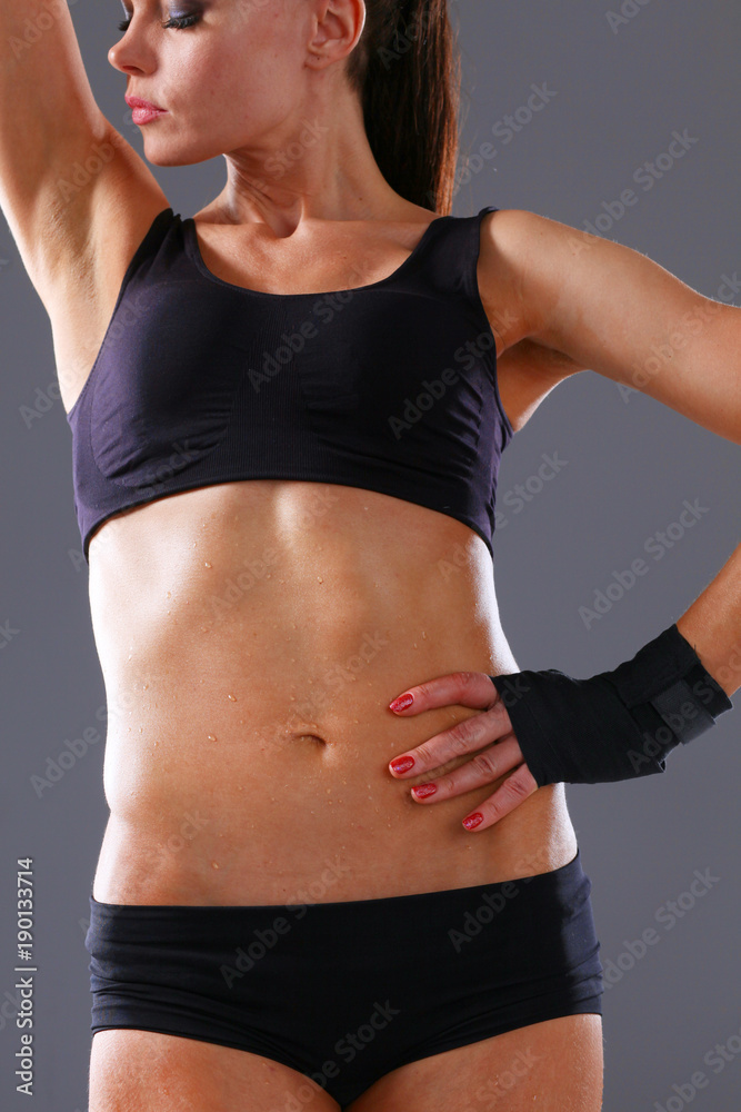 Muscular young woman standing on gray background. Muscular young woman Muscular young woman standing on gray background. Muscular young woman