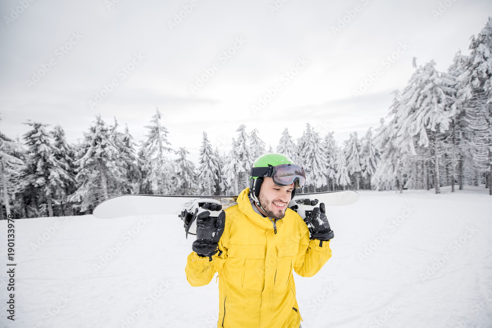 Man in yellow winter clothes walking with snowboard at the snowy mountains