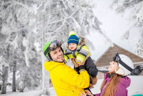 Happy family playing with baby boy standing in winter spots clothes outdoors during the winter vacations