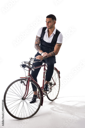 Portrait of young tattooed man in elegant clothes and shoes riding a bicycle. Studio shot. Full body shot