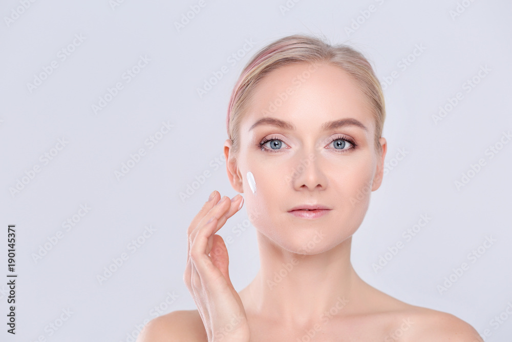 Portrait of happy smiling beautiful young woman touching skin or applying cream, isolated over white background