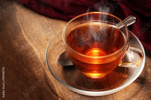 black tea freshly brewed in a glass cup, steaming hot drink on dark rustic wood, copy space