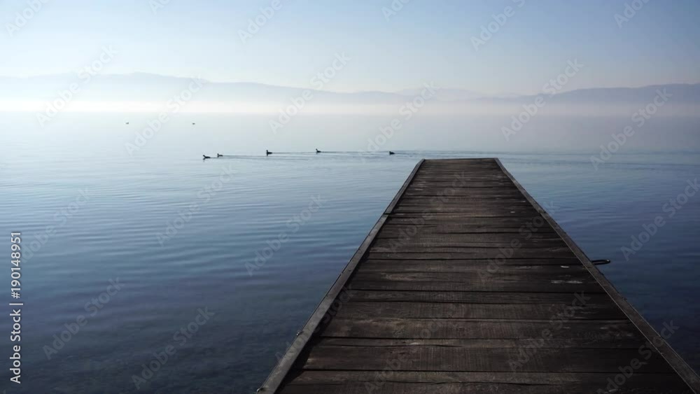 Wooden pier against ducks swimming in calm Ohrid Lake on sunny day, Macedonia Wooden pier against ducks swimming in calm Ohrid Lake on sunny day, Macedonia