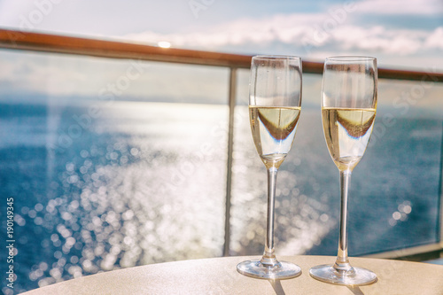 Luxury cruise ship travel champagne glasses on balcony deck with ocean sunset view on Caribbean vacation. Drinks in sun flare on cruise holiday destination.