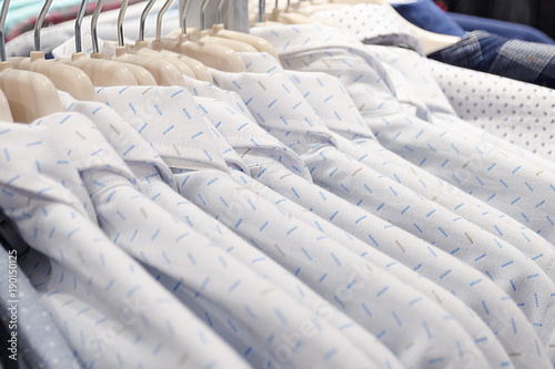 Men's shirts made of cotton light white color on the tremps in the store. Clothes sale. Photo with shallow depth of field.