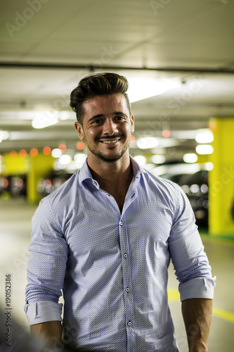 Handsome muscular man in casual clothing on background of underground parking.