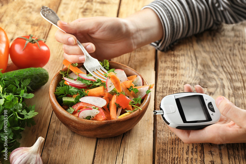 Woman holding digital glucometer while eating salad at table. Diabetes diet photo