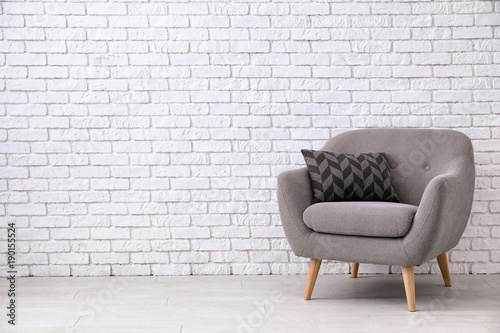 Comfortable armchair near white brick wall