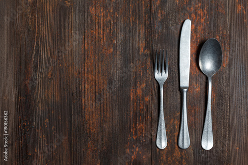 Old spoon and fork on brown wooden surface, empty space on the right, view from above