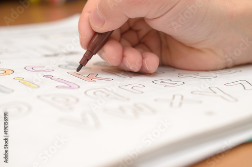 A child's hand writes and displays English letters in a notebook and alphabet with a pencil and felt-tip pen.