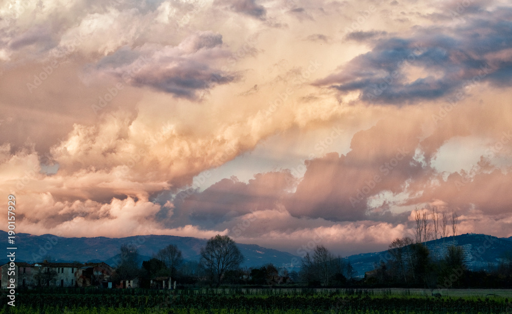 Landscape of clouds at sunset in the Padule di Fucecchio in Tuscany, Italy, with pink hues, well-defined clouds and countryside on the bottom
