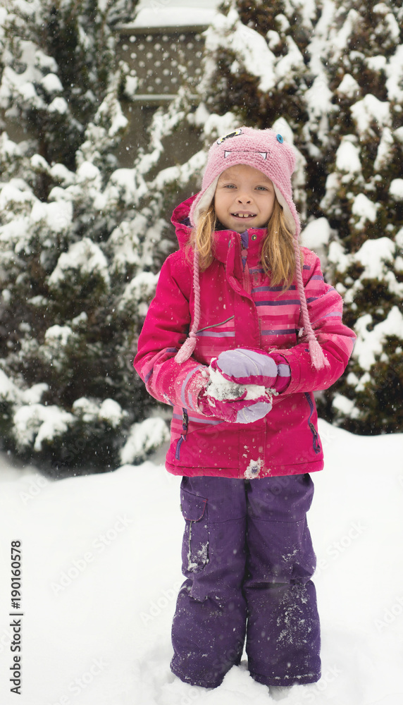 Little Caucasian blond girl is playing with snow on blur background