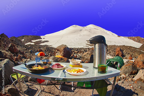 Tourist breakfast. High mountain summit camp located on stony moraine of glacier against the background of high snowy peak under clear blue sky. Early morning.