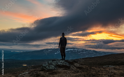 Man standing on rock facing scenic mountain sunset
